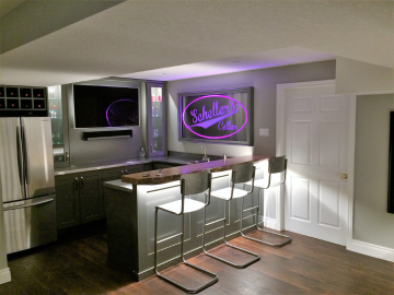 Modern Basement Bar With Seating Modern home bar with illuminated sign, wood countertop, and metal bar stools.