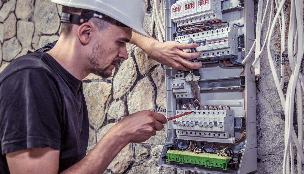 a male electrician works in a switchboard with an electrical connecting cable Electrician working on control panel outside a property.
